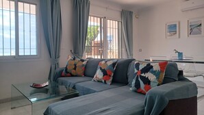 Sala de estar com sofá, mesa de centro de vidro e vista através de grandes janelas.