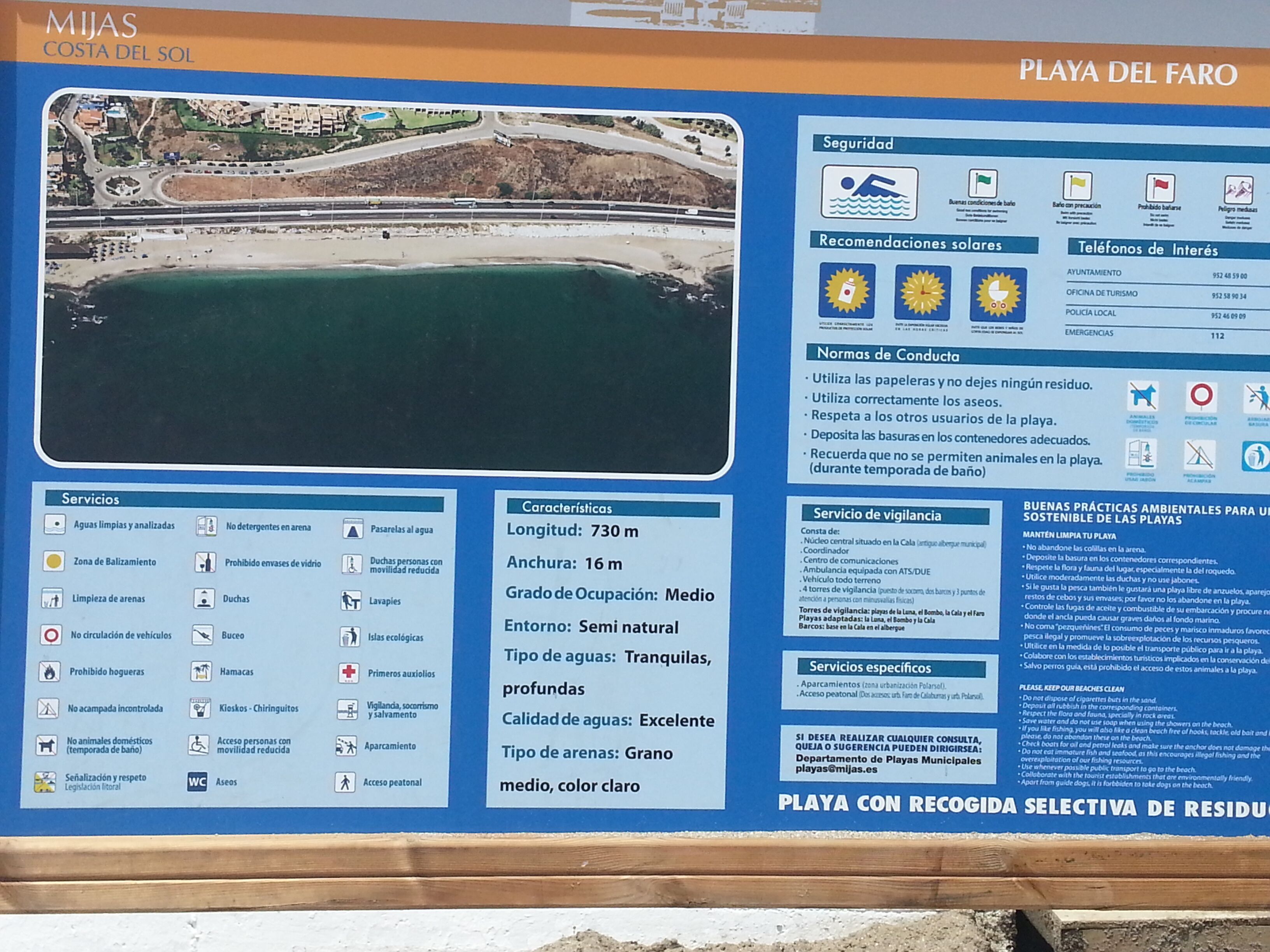 Eine Hinweistafel am Strand mit Informationen zu Annehmlichkeiten, Regeln und Notfallkontakten.