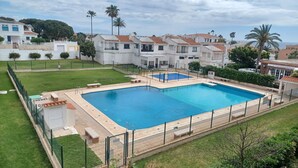 Piscina retangular com cerca ao redor, bancos e área gramada.