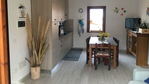 Une cuisine compacte dotée d’un four et d’un micro-ondes encastrés, un coin repas avec une table et des chaises, et un téléviseur posé sur un meuble en bois.