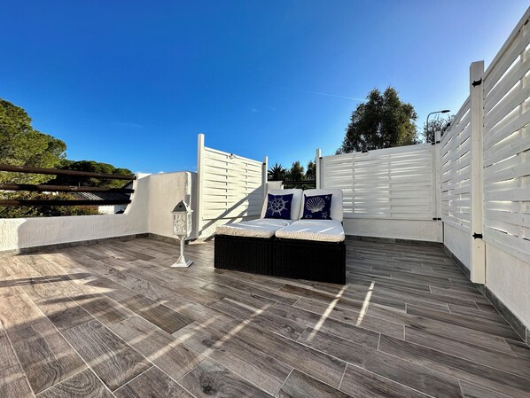 A rooftop terrace with a wooden floor, white walls, and a white fence.