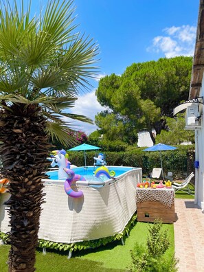 Ein Swimmingpool mit aufblasbaren Spielsachen, einer Palme und einer Holzterrasse mit Liegestühlen.