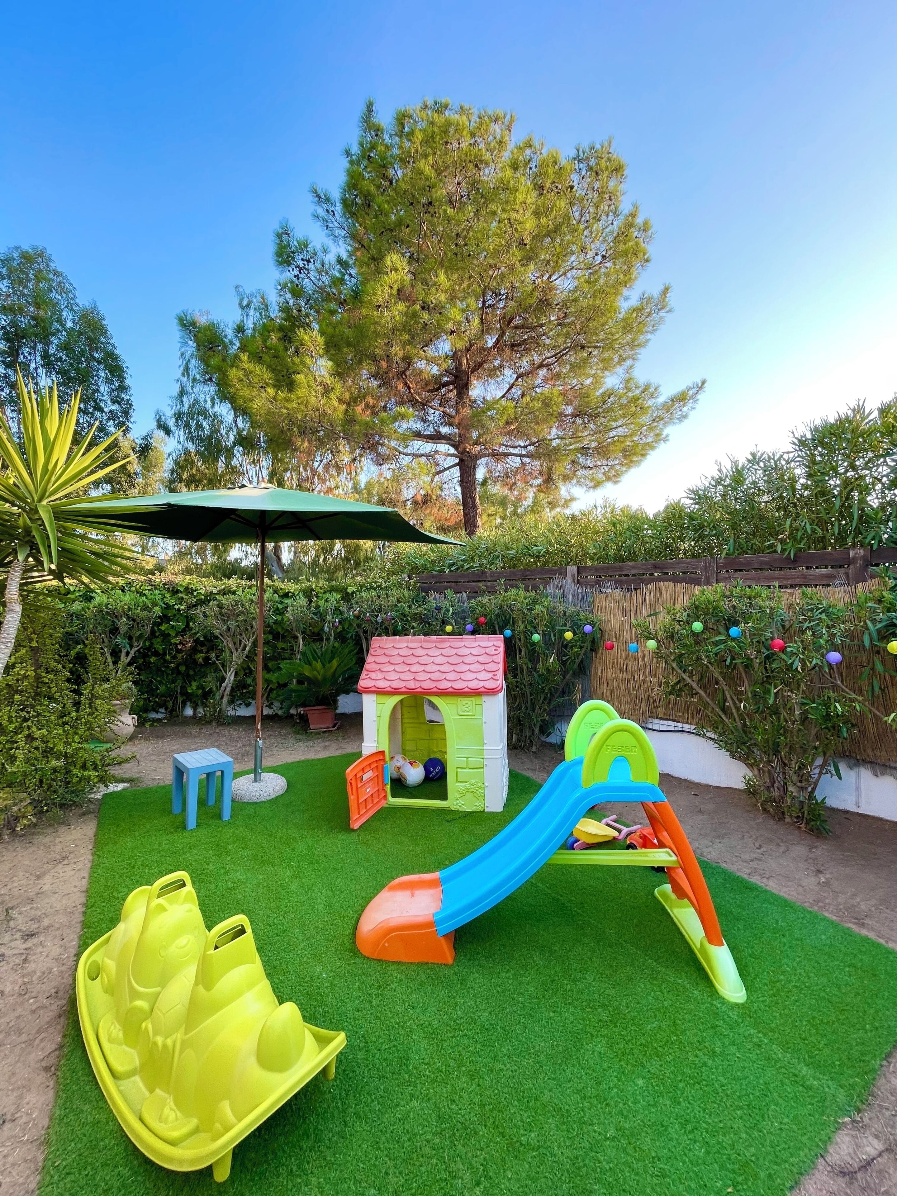 Zona de juegos infantiles con un tobogán, una casita y una mesa.