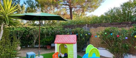 Zona de juegos infantiles con un tobogán, una casita y una mesa.