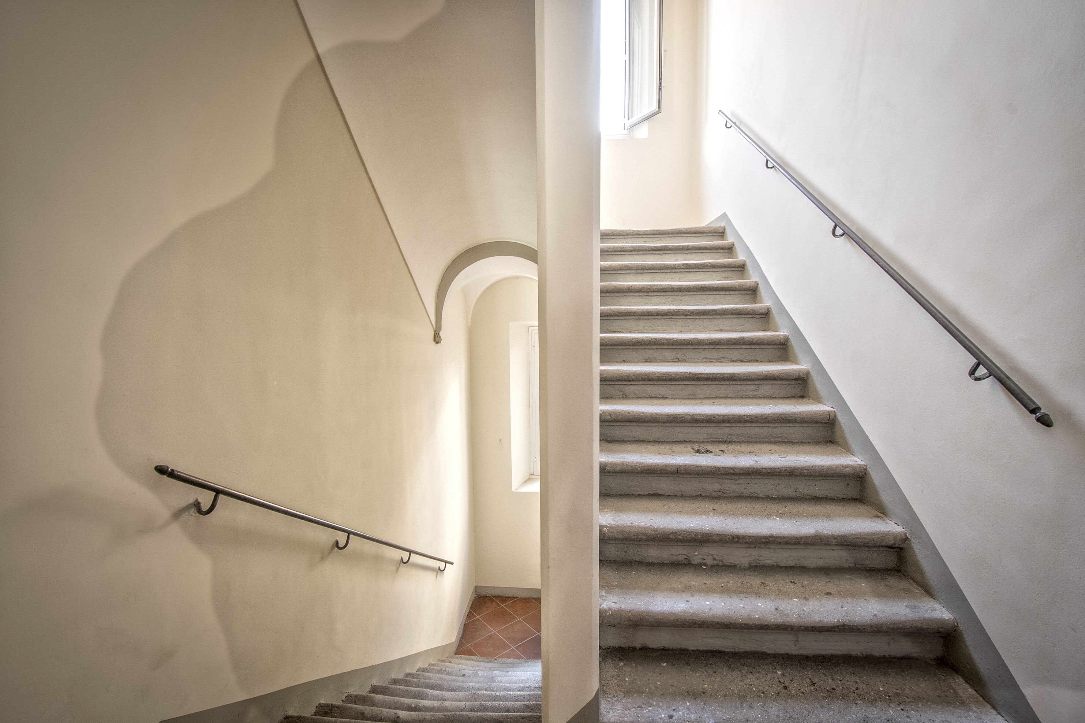 Una escala amb barana de metall, sòl de rajola i paret sense decorar.