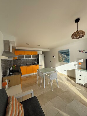 Een moderne keuken met oranje kastjes, een eethoek met witte stoelen en een woonkamer met een bank.