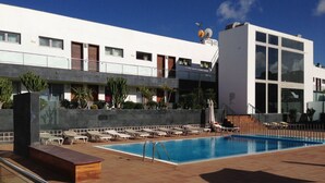 Un área de piscina en la azotea con sillones de descanso y un edificio moderno al fondo.