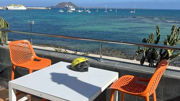 Terraza con mesa y sillas que ofrece vistas de la costa, con barcos y un barco llamado 'Fred Olsen'.