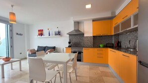 Una cocina moderna con armarios color naranja, una mesa de comedor blanca y sillas. Hay una estufa, un fregadero y una cafetera en la encimera.
