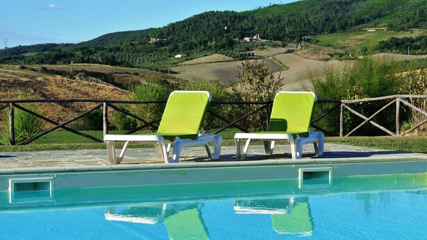 A swimming pool with two green lounge chairs and a view of a hilly landscape in the background. - Near San Gimignano Restored Air Conditioned Apartment with WiFi, Pool & Garden (San Gimignano Toscana)