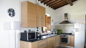 A kitchen with wooden cabinets, a microwave, a stove, and a refrigerator. - Near San Gimignano Restored Air Conditioned Apartment with WiFi, Pool & Garden (San Gimignano Toscana)