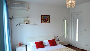 A bedroom with a bed, nightstand, lamp, air conditioner, artwork, mirror, and a door. - Studio apartment Julia with balcony in Lapad (Dubrovnik)