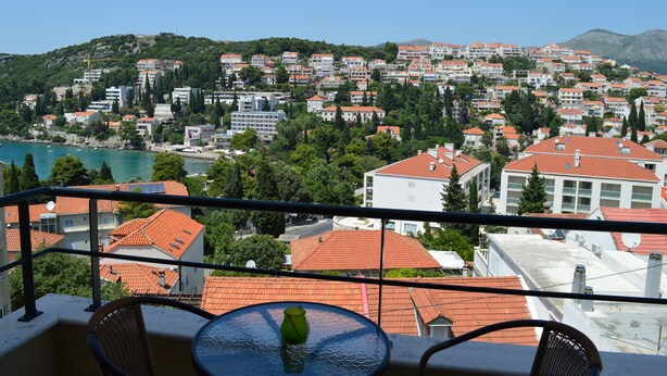 A balcony with a table and chairs overlooking a coastal town with red-roofed buildings and a view of the sea. - Studio apartment Julia with balcony in Lapad (Dubrovnik)