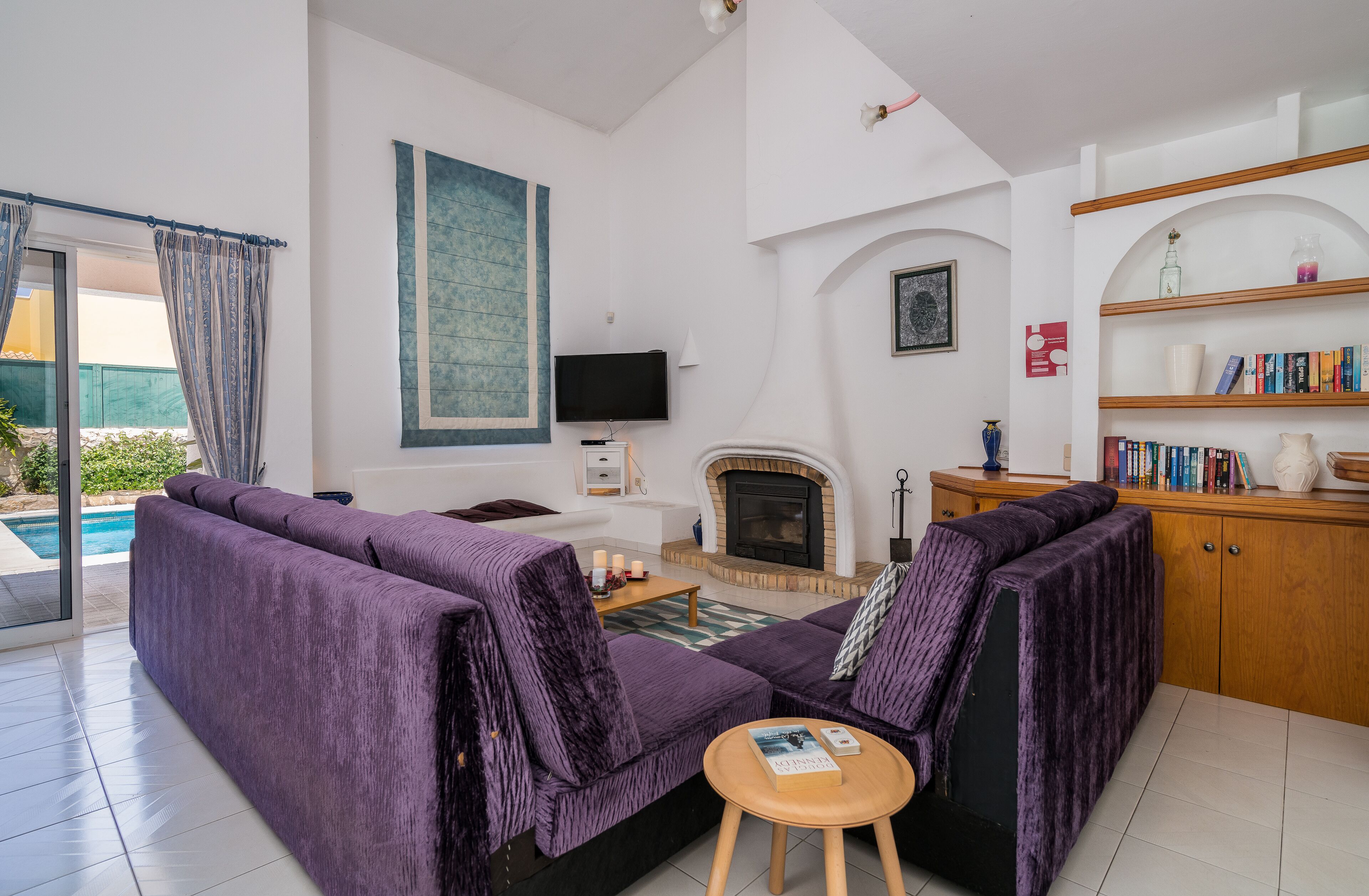 A modern living room with a purple sofa, a fireplace, a bookshelf, and a TV.