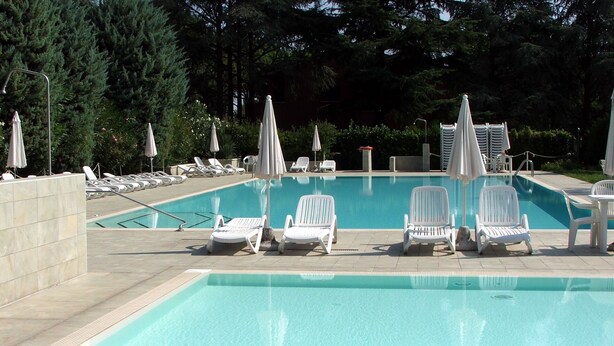 A swimming pool with white lounge chairs and umbrellas, surrounded by trees. - A6 Two-room apartment in a residence surrounded by greenery, with swimming pool (Sirmione)