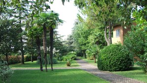 A well-maintained garden with a paved pathway leading to a building. - A6 Two-room apartment in a residence surrounded by greenery, with swimming pool (Sirmione)