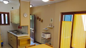 A compact kitchen with a dining area, a ceiling fan, a clock, and a microwave on a small shelf. - A6 Two-room apartment in a residence surrounded by greenery, with swimming pool (Sirmione)
