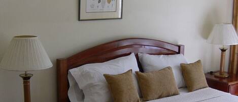 A neatly made bed with a wooden headboard, white and beige bedding, and two bedside lamps.