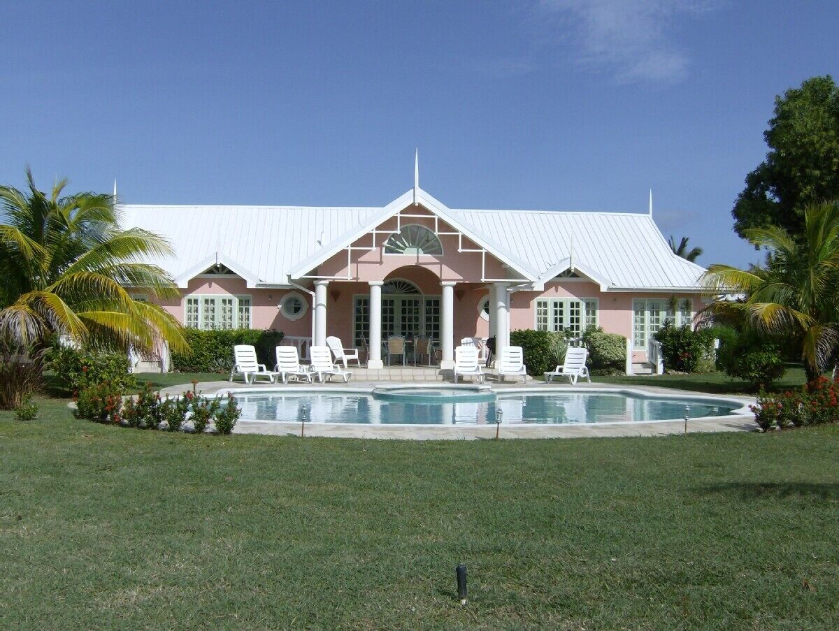 A large building with a swimming pool, surrounded by palm trees and a well-maintained lawn.