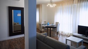 Ein modernes Wohnzimmer mit einer Couch, einem Esstisch mit Stühlen, einem Flachbildfernseher und einer Deckenleuchte.