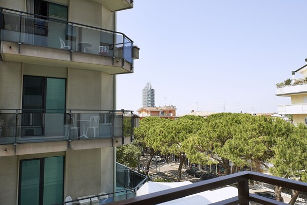 A multi-story building with balconies, a parking area, and a tree in the foreground.