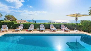 Une piscine dotée de chaises longues et d’un parasol, offrant une vue sur la côte.