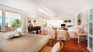 Un vaste espace de vie comprenant une table à manger, des chaises en osier, un canapé et un téléviseur.