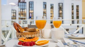 Ett frukostbord med croissanter, frukt och apelsinjuice på en balkong med utsikt över staden.