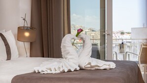 Ett hotellrum med en säng, en lampa, utsikt över staden och en konstnärlig dekoration gjord av handdukar.