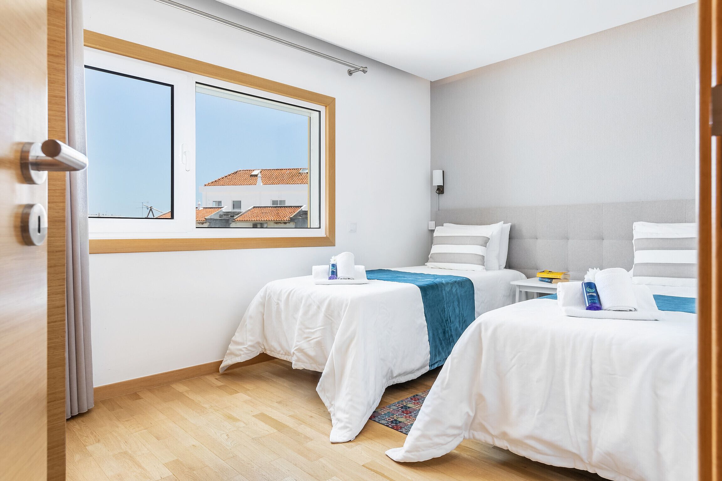 Habitación de hotel con dos camas, un ventanal grande y vista a edificios.