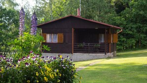 A wooden cabin with a red roof, surrounded by a well-maintained garden with various flowers and a stone pathway leading to it. - Log Cabins In The Beautiful Highlands Of Zeliv, By A Lake and forest. Oak cabin (Zeliv)