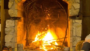 A stone fireplace with a fire burning inside, surrounded by stone walls and a wooden table. - Log Cabins In The Beautiful Highlands Of Zeliv, By A Lake and forest. Oak cabin (Zeliv)