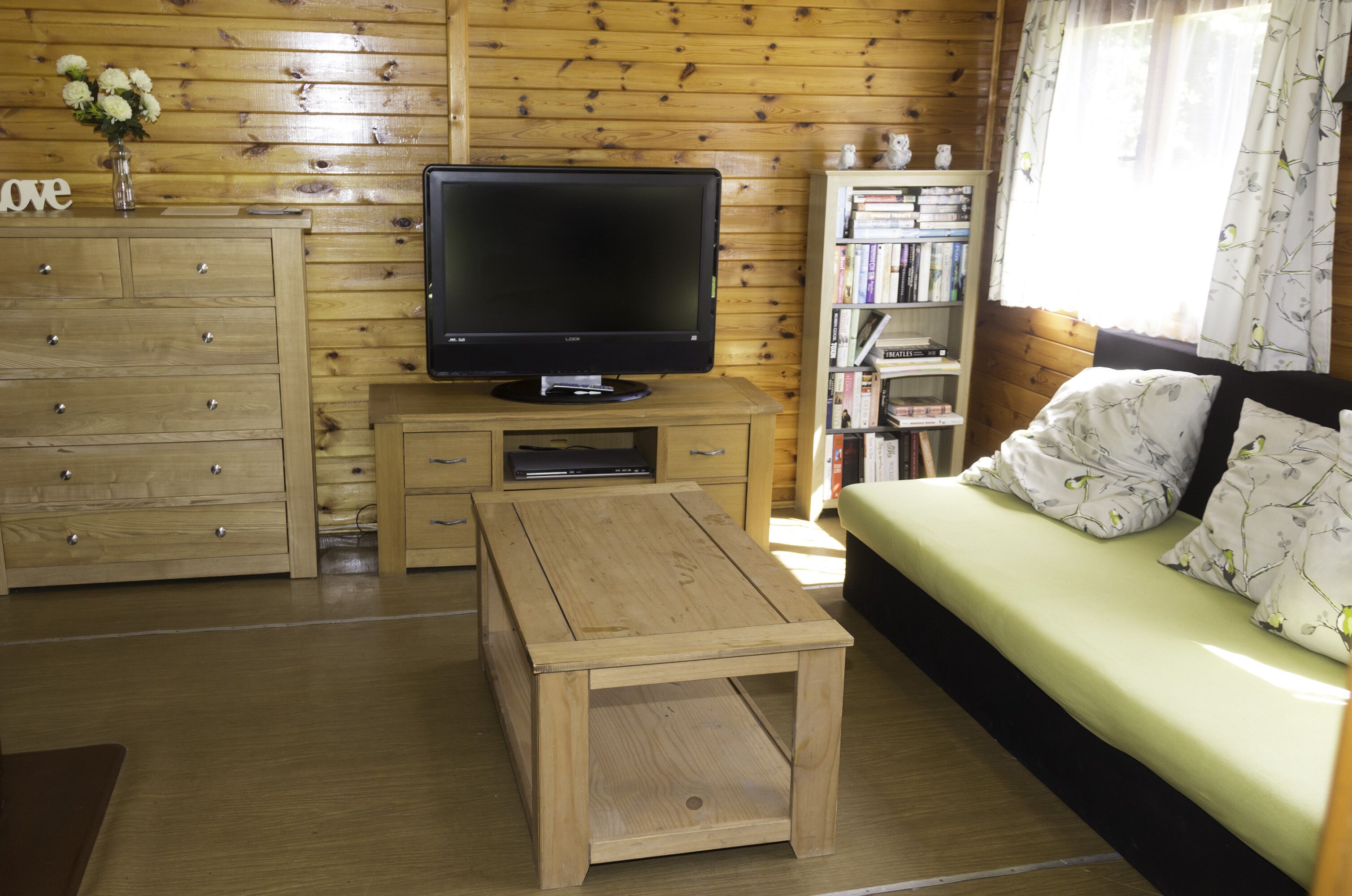 A cozy room with a wooden TV stand, a sofa, a bookshelf, and a small table.