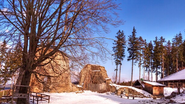 A snow-covered outdoor area with a wooden bench, stone structures, and a wooden building. - Log Cabins In The Beautiful Highlands Of Zeliv, By A Lake and forest. Oak cabin (Zeliv)
