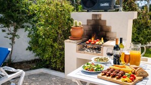 An outdoor grill with food, a table with drinks, and a chair. - Beautiful 4 Bedroom Villa Silva, Private Pool, Close To The Strip And Old Town (Albufeira)