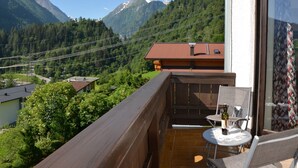 Un balcón con una mesa y sillas, con vista a un paisaje montañoso con casas y líneas eléctricas.