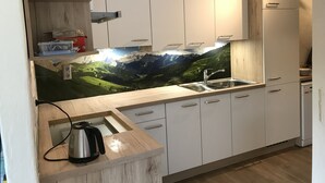 Cocina moderna con armarios blancos, encimera de madera y un mural con vistas a la montaña.