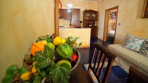 A dining area with a table set for two, a sofa with patterned cushions, and a kitchen in the background. - VILLA SEA SALENTO (Marina San Gregorio)