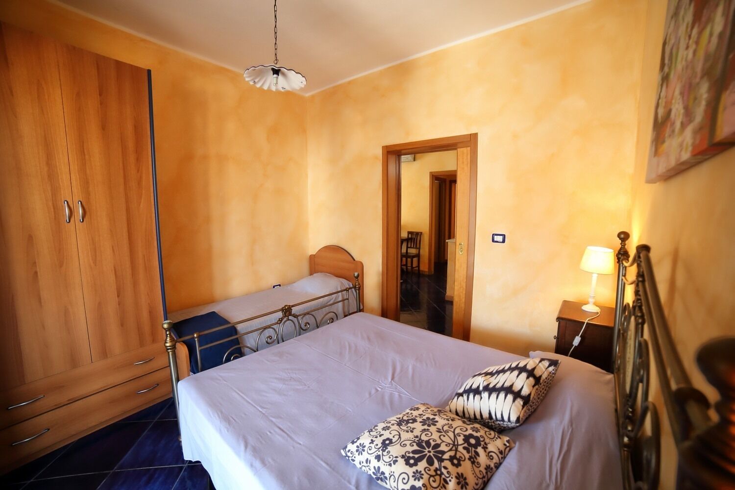 A bedroom with a bed, a wardrobe, a nightstand, and a lamp.
