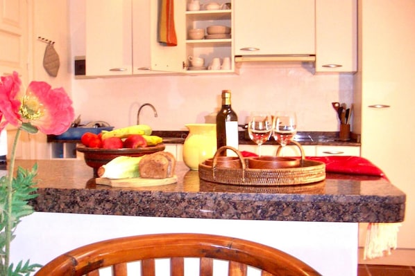 A kitchen counter with fruits, a bottle, glasses, and a chair.