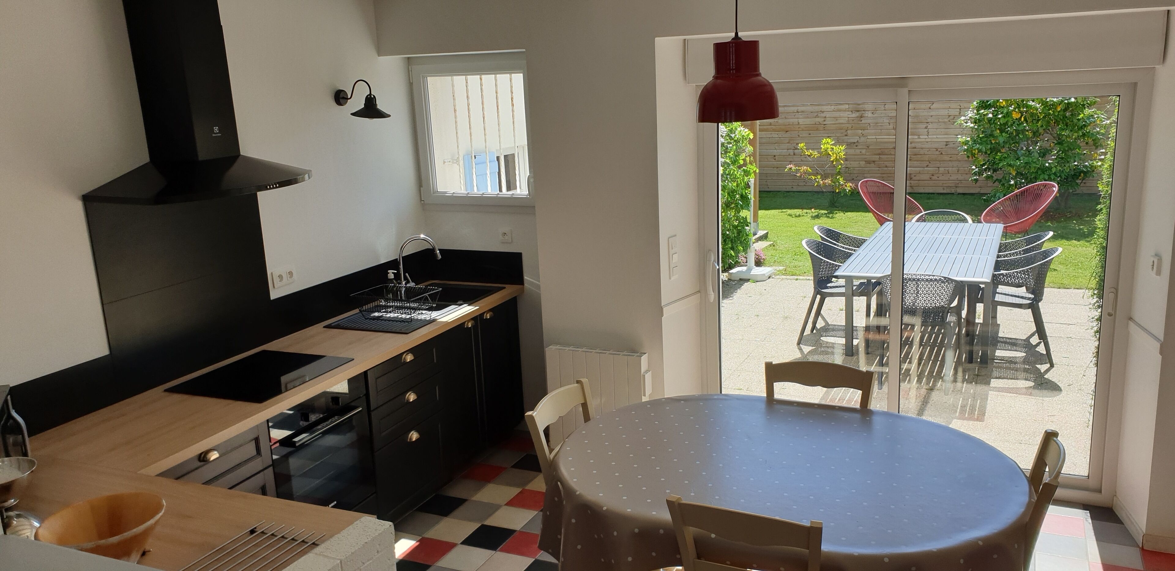 A modern kitchen with a black stove, a sink, and a window. There is a dining area with a table and chairs outside.