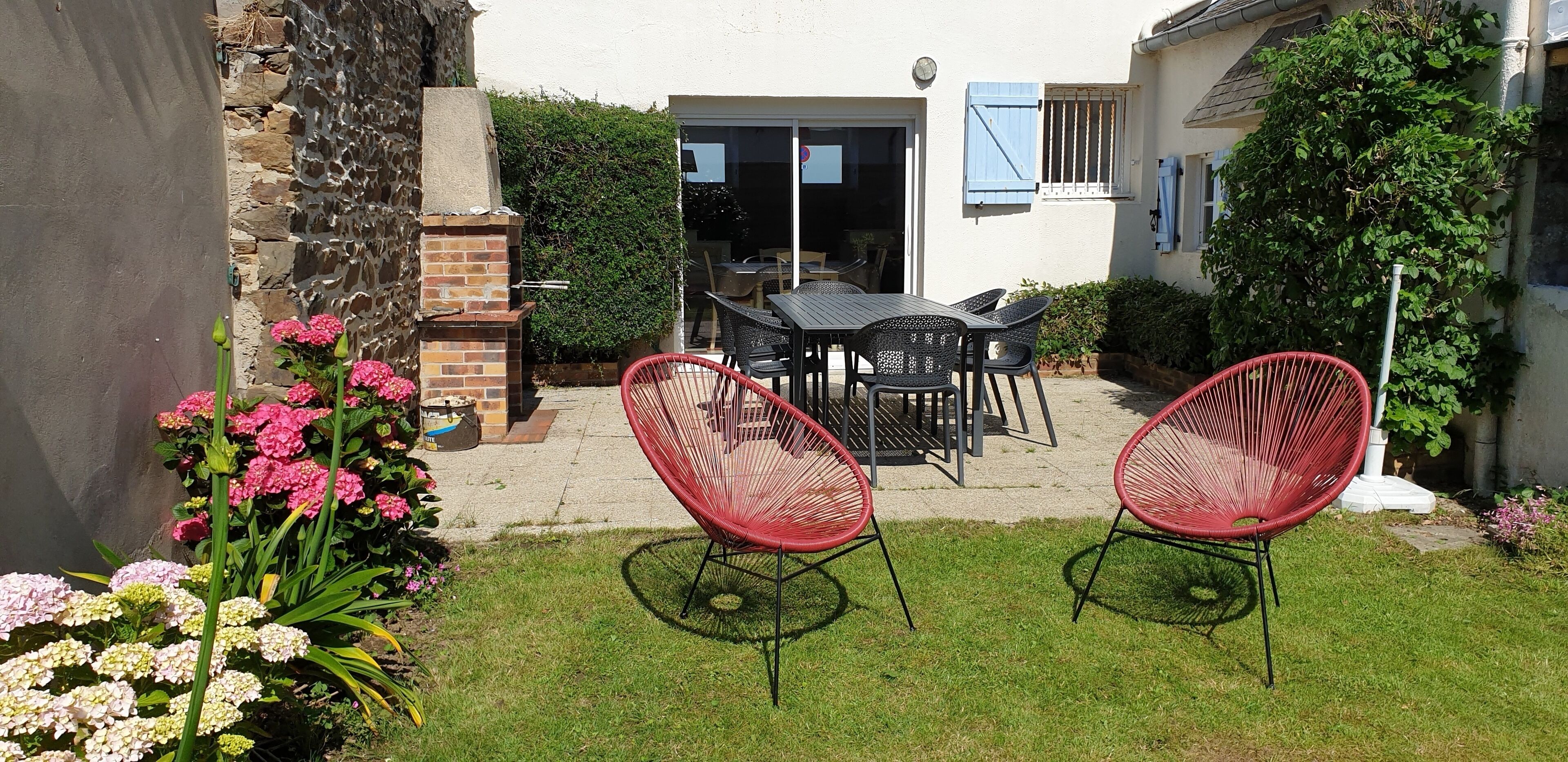 Une terrasse avec un barbecue en briques, une table avec des chaises et un jardin fleuri.