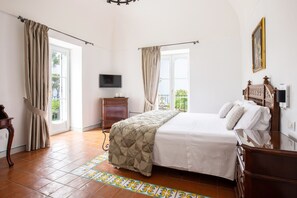 A bedroom with a bed, curtains, a television, a dresser, and a window with a view.