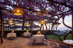 An outdoor dining area with round tables and chairs, surrounded by trees and a hammock. - AMORE RENTALS - Villa Jasmine with Private Pool Ideal for Weddings (Sant´Agata sui Due Golfi)