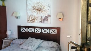 Une chambre à coucher avec un lit, une table de chevet, une lampe fixée au mur et un tableau.