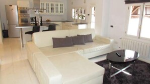 Una sala de estar moderna con un sofá blanco, una pequeña mesa redonda de centro y una cocina al fondo.
