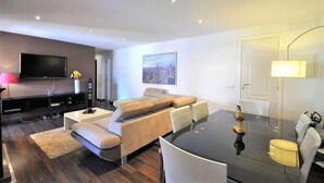 Una sala moderna con un televisor de pantalla plana, un sofá, una mesa de comedor y una lámpara.