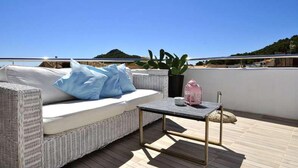 Una terraza en la azotea con un sofá de mimbre, una mesita, una planta en maceta y una jaula de pájaros.