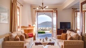 A living room with a sofa set, a television, and a view of a cityscape through an open door. - Luxury stone-made villa with exceptional view & pool (Lefkada)