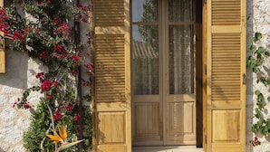 A wooden door with shutters, a stone wall, and a small garden with red flowers and a bird of paradise plant. - Luxury stone-made villa with exceptional view & pool (Lefkada)